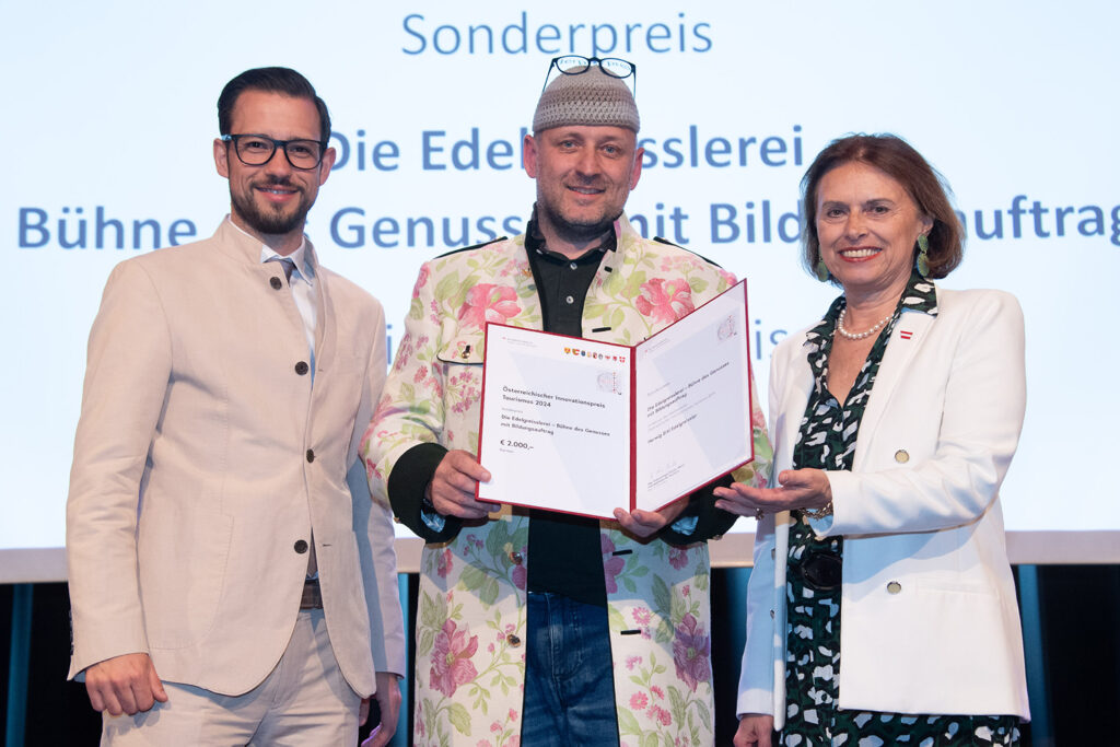 Landesrat Sebastian Schuschnig (re.) und Tourismus-Staatssekretärin Susanne Kraus-Winkler überreichen den Sonderpreis an Herwig Ertl. © BMAW/StudioHorst